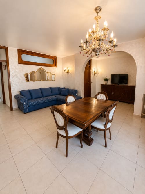 Elegante zona living e pranzo in Appartamento Lisa con divano blu, tavolo in legno, lampadario e entrata ad arco