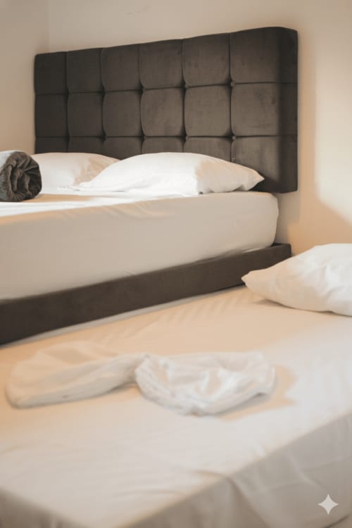 Dormitorio moderno en Olamar Living Coveñas con cabecero tapizado oscuro, almohadas blancas y ropa de cama beige con vista al jardín