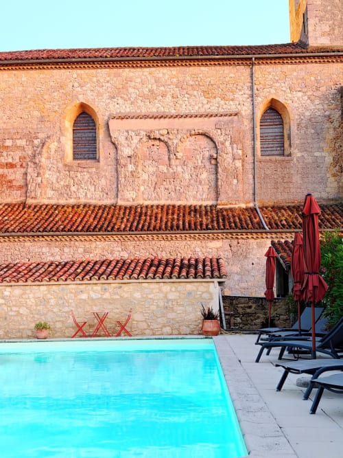 Le Rêve d'Alice à Saint-Puy avec piscine turquoise, bâtisse en pierre aux toits de terre cuite et chaises longues rouges