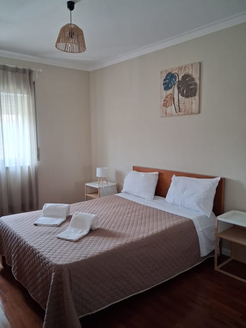 Helles Schlafzimmer in der Furnaka Village Herberge in Lourinhã mit Queensize-Bett, Holzkopfteil, gewebtem Hängeleuchte und tropischen Blättern