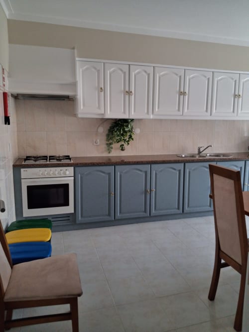 Moderne Küche mit weißen Oberschränken und blauen Unterschränken, Gasherd und Arbeitsplatte im Apartment Tininha da Ilha