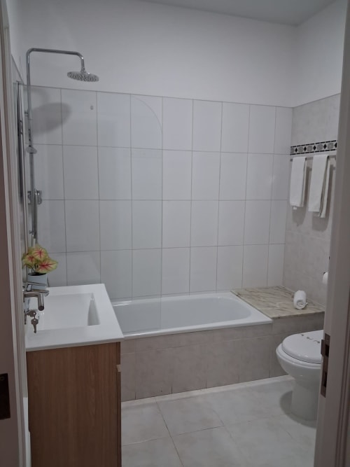 Modernes Badezimmer in der Furnaka Village Herberge in Lourinhã mit weißen Fliesenwänden, Badewanne, Waschbecken, Toilette und Dusche