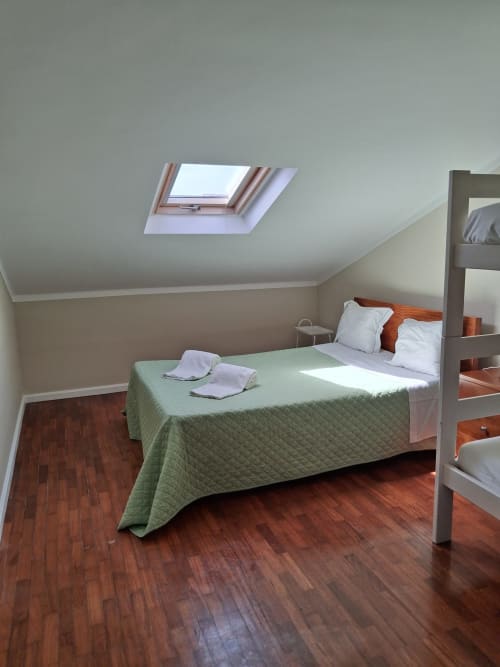 Helles Dachzimmer mit Dachfenster in der Furnaka Village Herberge in Lourinhã, Holzböden und grüne Bettdecke