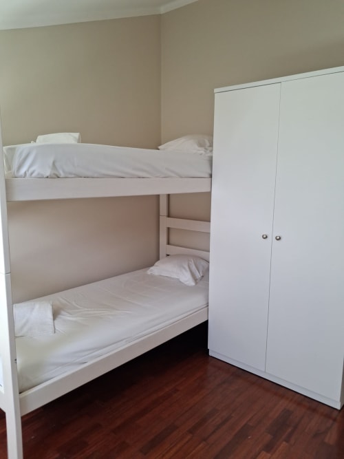 Weiße Etagenbetten mit weißer Bettwäsche in einem Mehrbettzimmer der Furnaka Village Herberge in Lourinhã, mit Kleiderschrank und Holzboden.