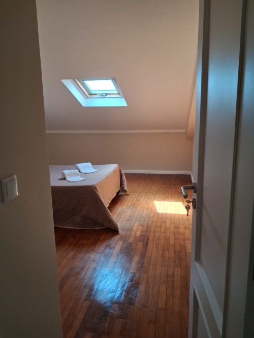 Gemütliches Dachzimmer in der Furnaka Village Herberge mit Dachfenster, Holzböden und Bett mit blauen Kissen in der Nähe des Strandes von Peniche