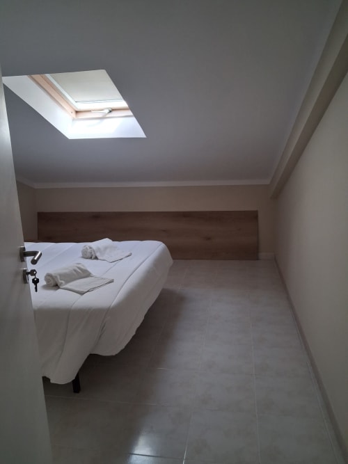 Minimalistisches Dachzimmer in der Herberge Furnaka Village in Lourinhã mit Dachfenster, Holzkopfteil, weißer Bettwäsche und Fliesen