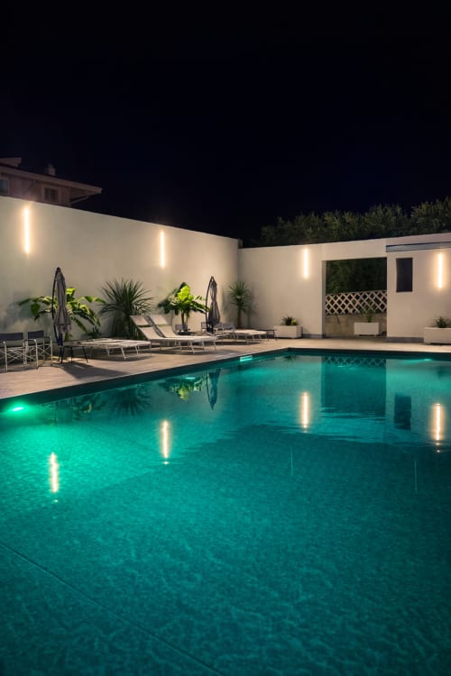 Piscina illuminata di notte con lettini, pareti bianche e piante tropicali a Trabocchi Livings, Ortona