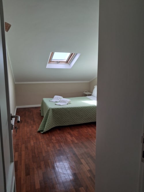 Helles Dachzimmer in der Herberge Furnaka Village in Lourinhã mit Dachfenster, Holzboden und grüner Bettwäsche