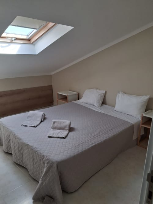 Helles Dachgeschoss-Schlafzimmer im Furnaka Village Hostel mit Dachfenster, Queensize-Bett, weißen Kissen, Holzkopfteil und minimalistischem Design