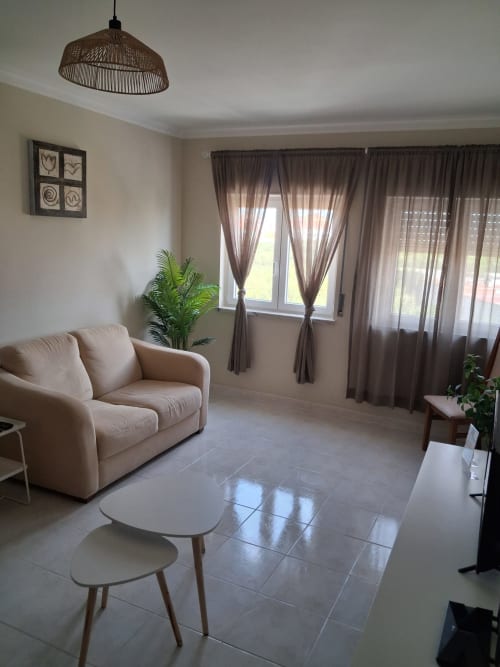 Modernes Wohnzimmer der Wohnung Tininha da Ilha in Lourinhã mit beigem Sofa, Pendelleuchte und Terrassenblick