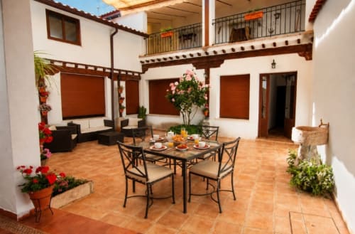 Patio amplio de la Casa Rural La Herrería con suelos de barro cocido, mesa de comedor, zona de estar y plantas en flor