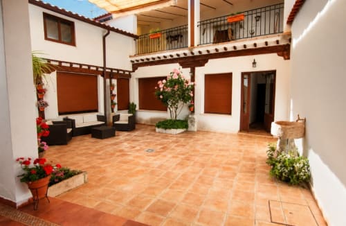 Patio de la Casa Rural La Herrería con suelo de barro, vigas de madera, plantas en flor y zona de descanso