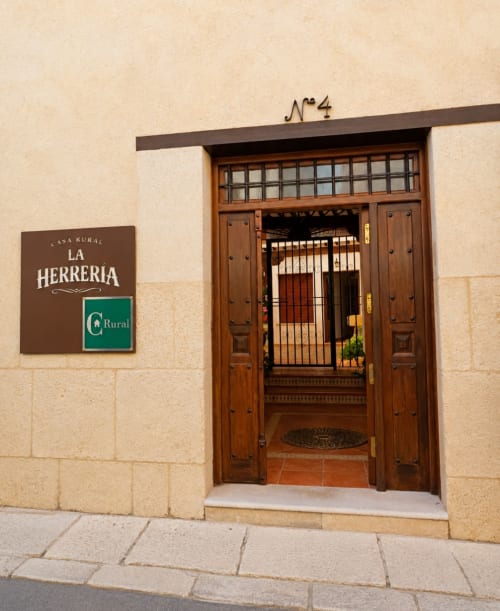 Entrada a la Casa Rural La Herrería con puerta de madera, número 4 y letrero en fachada de piedra color crema