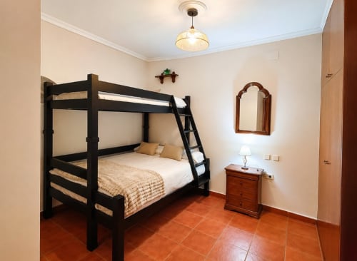Cama litera negra en dormitorio rústico de la casa rural La Herrería con suelo de terracota y mesita de madera