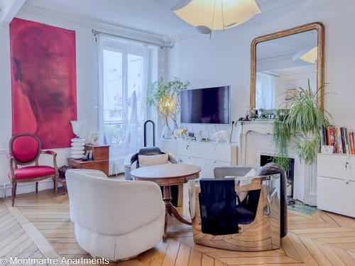 Montmartre Apartments Paris - Paradis Artistique living room with pink velvet chair, fireplace, TV, and wooden herringbone