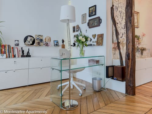 Modern Parisian apartment workspace with glass desk, white storage, parquet flooring, and artistic décor at Montmartre