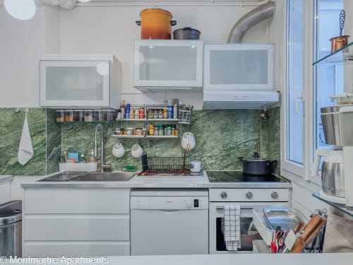 Modern kitchen in Montmartre Apartments Paris with white cabinets, green marble backsplash, and stainless steel appliances