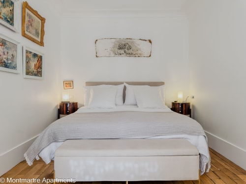 Bright bedroom in Montmartre Apartments Paris with queen bed, white bedding, wooden nightstands, and vintage wall art