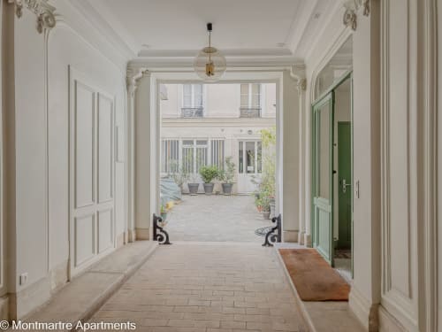 Elegant hallway of Montmartre Apartments in Paris with white classical doors, pendant light, and courtyard view with potted