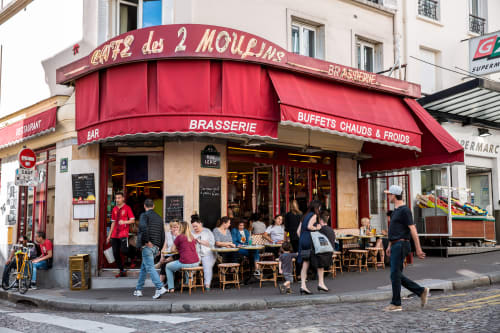 Café des 2 Moulins brasserie in Montmartre, Paris with red awning, outdoor seating, and bustling street scene
