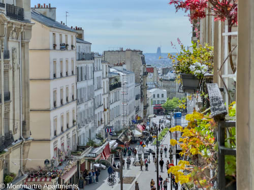 View from Montmartre Apartments balcony overlooking bustling Parisian street with historic buildings and Sacré-Cœur in