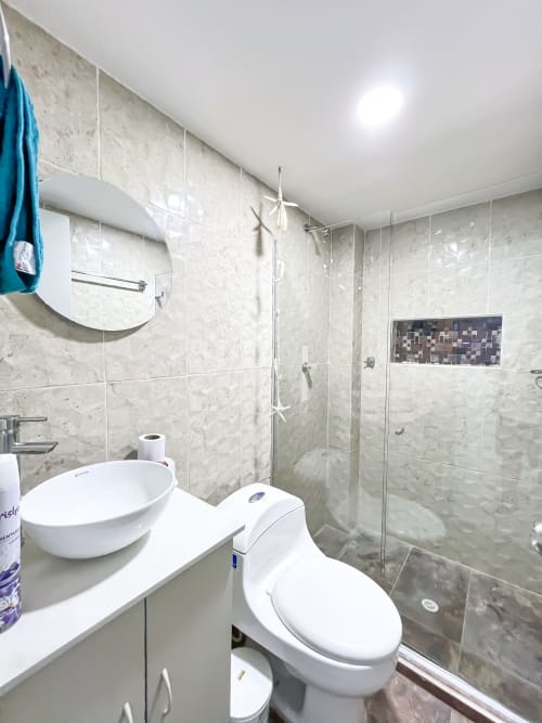 Baño moderno en Olamar Living con lavamanos tipo vasija, inodoro y cabina de ducha con cristal
