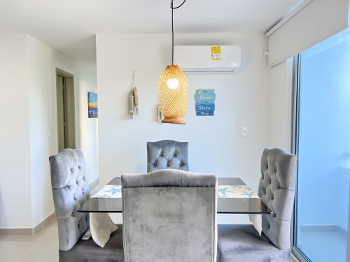 Comedor moderno del apartamento Mar Azul en Olamar Living, Coveñas con sillas tapizadas grises y lámpara colgante tejida