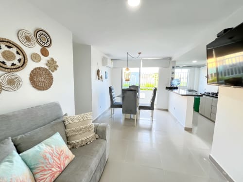 Apartamento moderno de planta abierta en Olamar Living con sofá gris, mesa de comedor, cocina y placas decorativas en la pared