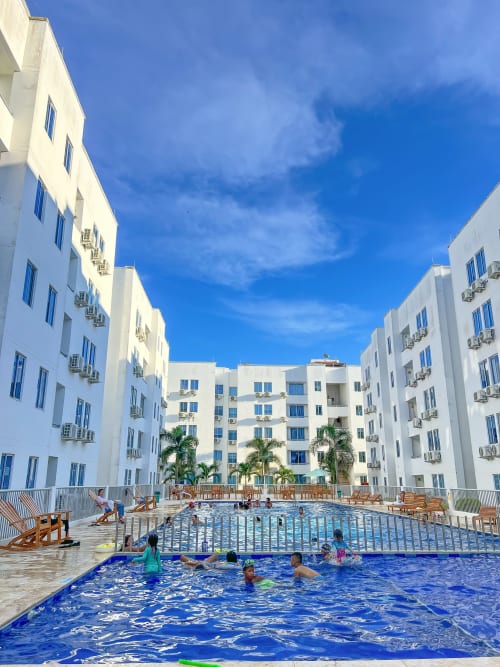 Patio del hotel Olamar Living en Santiago de Tolú con dos piscinas, edificios blancos y palmeras bajo cielo azul