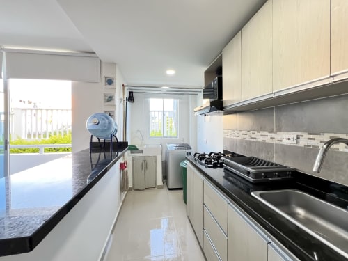 Cocina moderna en apartamento Mar Azul de Olamar Living, Coveñas, con gabinetes de madera clara, encimeras negras, estufa y lavaplatos