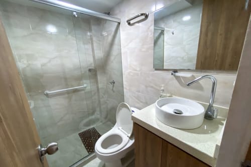 Baño moderno en Olamar Living Coveñas con lavabo de cerámica blanca, inodoro, ducha con cristal y espejo.