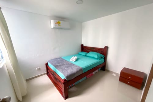 Dormitorio luminoso en Olamar Living, Coveñas, con ropa de cama turquesa, cama de madera, aire acondicionado y decoración minimalista