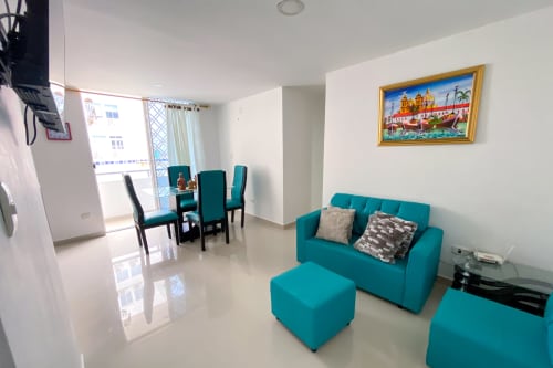 Luminosa sala de estar en Celeste Apartamento Coveñas con sofá turquesa, comedor y amenidades modernas