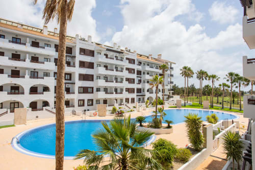 Apartamento Haus Holiday Homes con vista a piscina curva, palmeras y edificios blancos en Los Alcázares