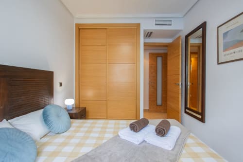 Moderno dormitorio con puertas de madera, almohadas azules y toallas enrolladas en Haus Holiday Homes de Los Alcázares