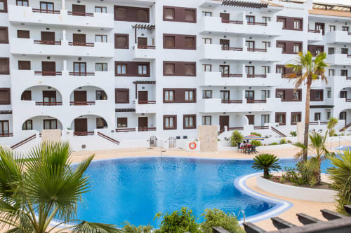 Piscina del apartamento Haus Holiday Homes con edificio blanco, palmeras y tumbonas en Los Alcázares