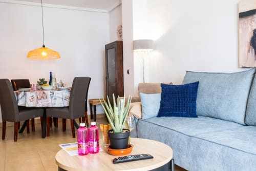 Moderna sala de estar en Haus Holiday Homes, Los Alcázares, con sofá azul, mesa comedor y lámpara colgante ámbar