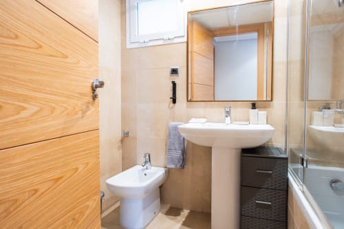 Baño moderno en apartamento de Haus Holiday Homes, Los Alcázares, con lavamanos pedestal blanco, bidé, puerta de madera y cristal