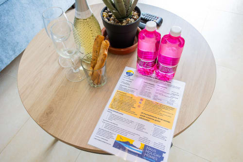Amenidades de bienvenida en mesa redonda: vino, copas, palitos de pan, cactus y botellas rosas en Haus Holiday Homes Los Alcázares