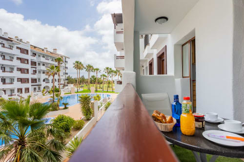 Balcón con mesa de desayuno con vistas a la piscina y jardines de palmeras en Haus Holiday Homes, Los Alcázares