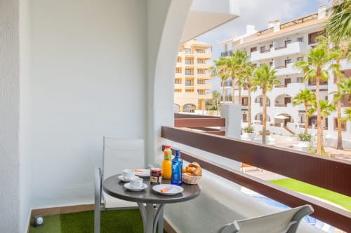 Balcón del apartamento en Haus Holiday Homes con mesa de desayuno con vistas a la piscina y palmeras de Los Alcázares
