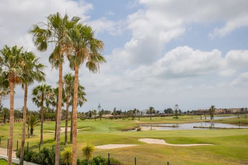Campo de golf bordeado de palmeras con campos verdes y obstáculos de agua en Haus Holiday Homes, Los Alcázares