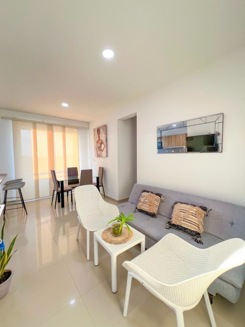 Moderna sala de estar en Coveñas con sofá gris, sillas blancas, mesa de comedor, TV y abundante luz natural