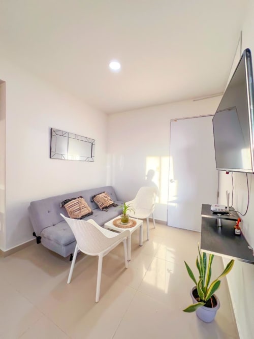 Moderno salón de apartamento en Olamar Living, Coveñas, con sofá gris, sillas blancas, televisor y plantas decorativas