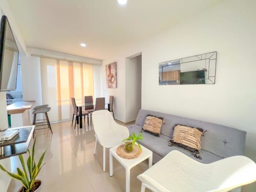 Moderna sala de estar en Olamar Living, Coveñas, con sofá gris, sillas blancas y comedor junto a ventanales