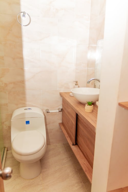 Baño moderno con inodoro blanco, lavamanos redondo sobre tocador de madera y paredes con baldosas beige en Olamar Living, Coveñas