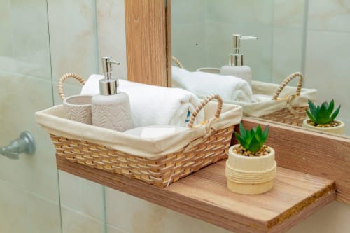 Tocador de baño con cestas tejidas conteniendo toallas blancas, dispensadores de jabón y pequeñas suculentas en maceta en Olamar Living,