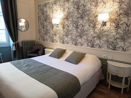 Chambre élégante du Pavillon Saint Martin avec papier peint à motifs de palmiers, literie blanche et mobilier moderne
