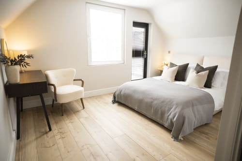 The Oriel Loft bedroom at Stay at Wellington Circus, Nottingham, featuring a bed with grey bedding, cream chair, desk, and