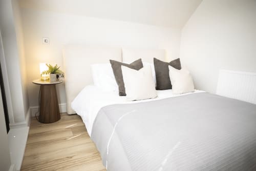 Modern bedroom at Stay Wellington Circus, Nottingham with white bedding, grey accent pillows, wooden nightstand and warm